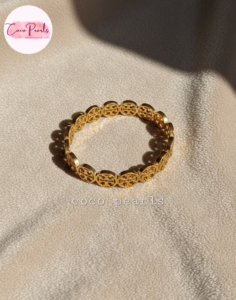 coco pearls stainless steel anti tarnish gold interlocking logo handcuff with all over logos connected displayed on a velvet cloth