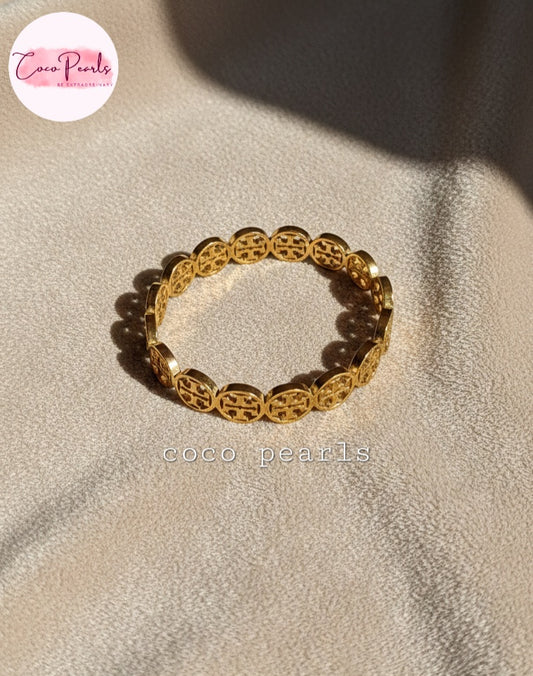 coco pearls stainless steel anti tarnish gold interlocking logo handcuff with all over logos connected displayed on a velvet cloth