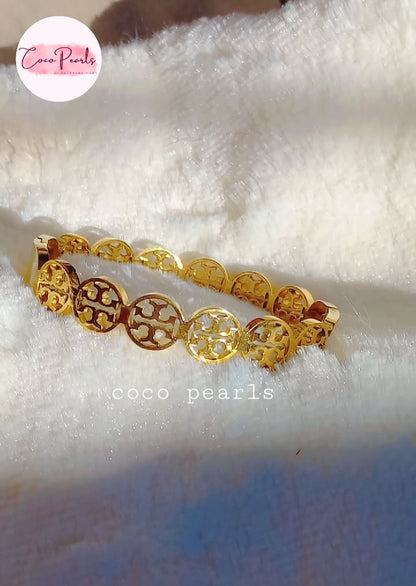 coco pearls stainless steel anti tarnish gold interlocking logo handcuff with all over logos connected displayed on a white cloth