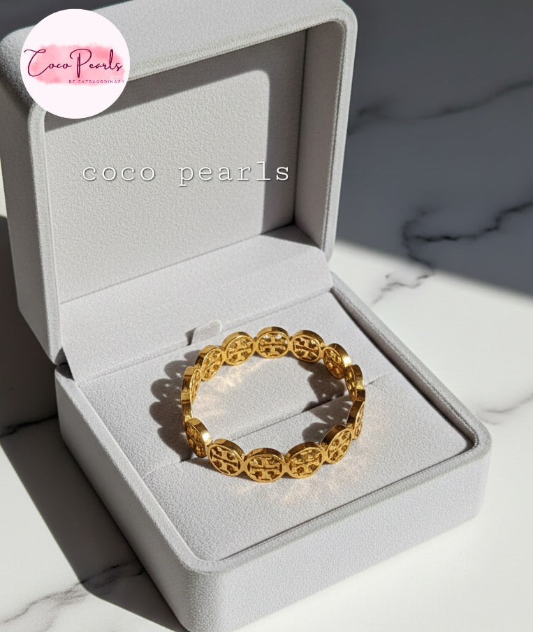 coco pearls stainless steel anti tarnish gold interlocking logo handcuff with all over logos connected displayed on a jewelry box