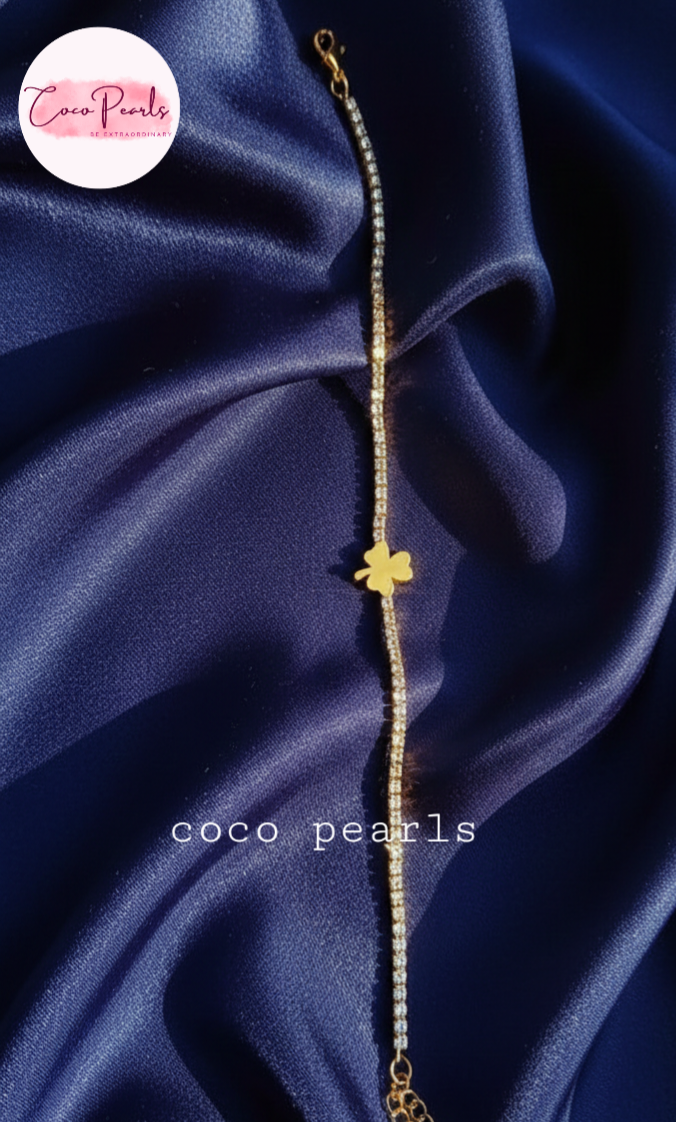 coco pearls stainless steel anti tarnish lucky charm bracelet. diamond studded with golden clover in center displayed on blue background