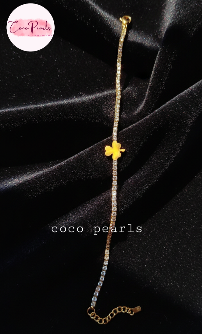coco pearls stainless steel anti tarnish lucky charm bracelet. diamond studded with golden clover in center displayed on black background