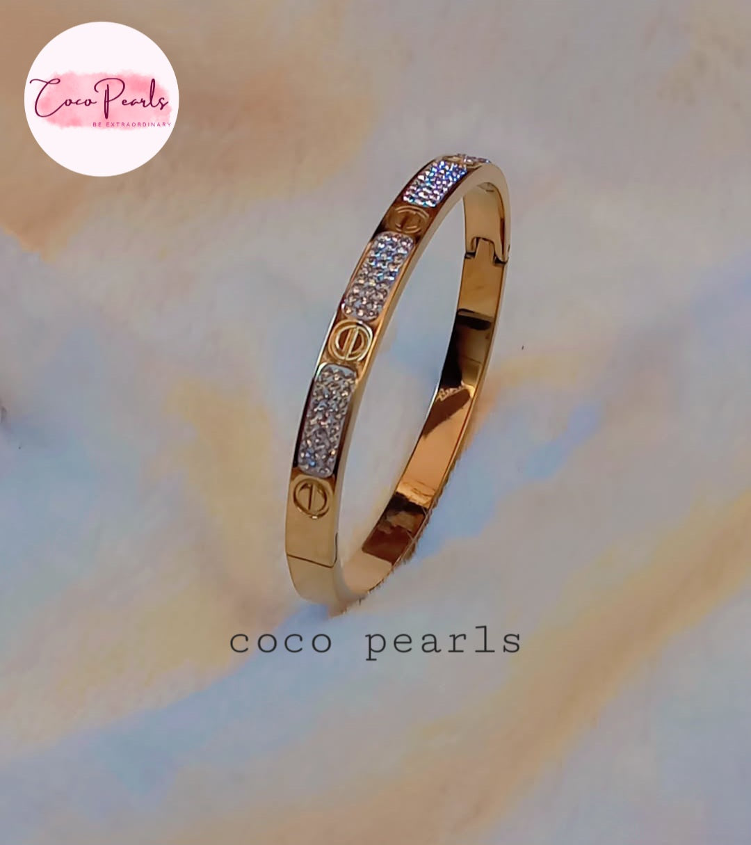 Coco Pearls Stainless Steel Anti Tarnish Gold lucky charm bangle with embedded diamonds on a soft, multicolored background