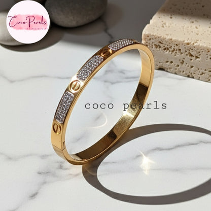Coco Pearls Stainless Steel Anti Tarnish Gold lucky charm handcuff bracelet with diamond accents on a marble surface