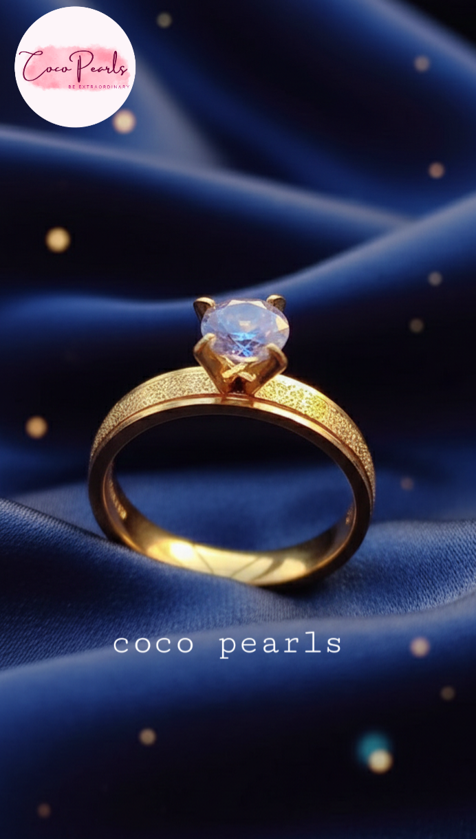 coco pearls stainless steel anti tarnish Gold solitaire ring with a clear gemstone on a dark surface