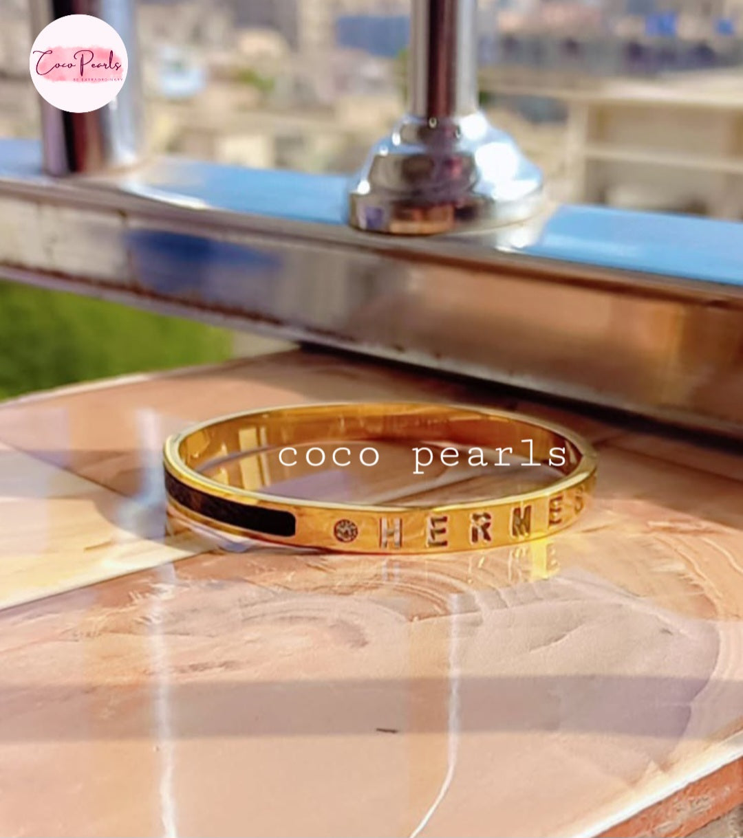 Coco Pearls Stainless Steel Anti Tarnish Gold  lunar glow handcuff bangle bracelet with 'HERMES' engraving on a reflective surface 