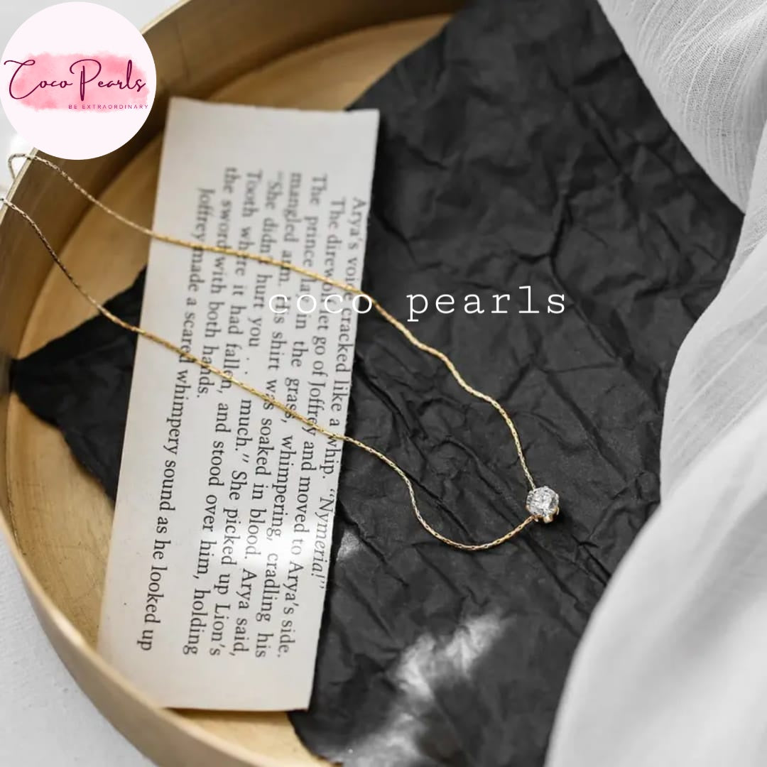 Coco Pearls Stainless Steel Anti Tarnish Gold milestone necklace with a stone pendant on a book page, branded