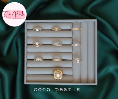 Set of gold rings in a display box with 'Coco Pearls' branding on a green satin background.
