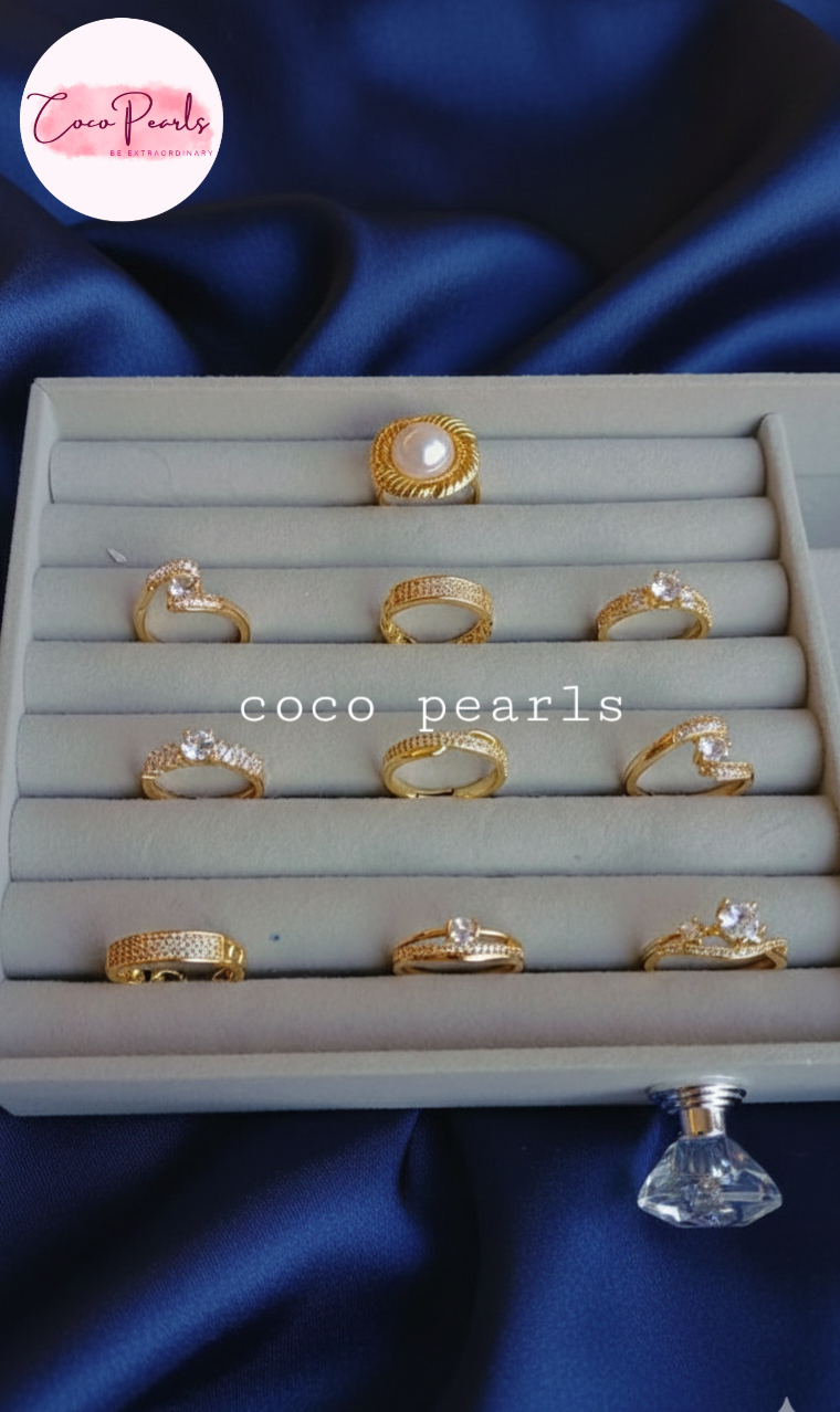 Gold rings with pearls on a display tray against a blue satin background, branded 'Coco Pearls'.