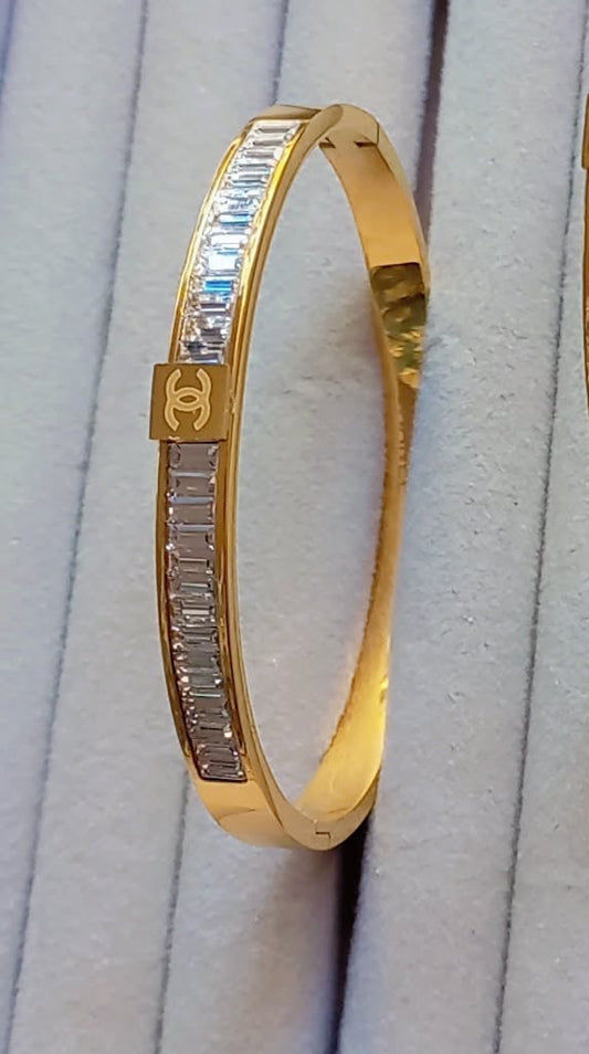 Coco pearls stainless Steel anti tarnish Waterproof gold aura diamond line handcuff bangle with embedded stones on a white cushioned surface.
