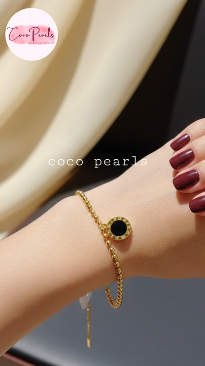 Coco Pearls Stainless Steel Anti tarnish Golden roman bead bracelet with bead chain and double sided roman hanging charm. one side white one side black. displayed on hand