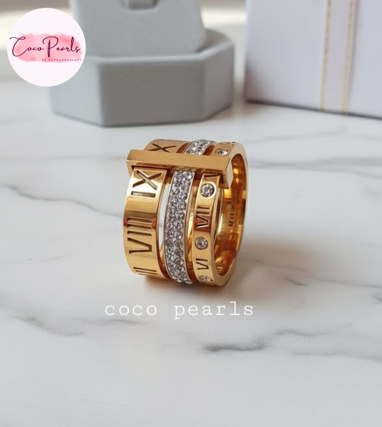 Coco Pearls Stainless Steel Anti Tarnish Gold roman trio ring with three engraved numbers and diamonds bands displayed on a marble surface