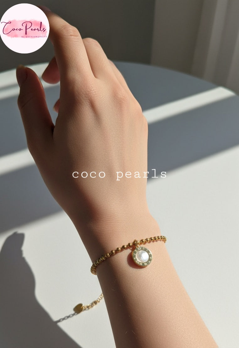 Coco Pearls Stainless Steel Anti tarnish Golden roman bead bracelet with bead chain and double sided roman hanging charm. one side white one side black. displayed on hand