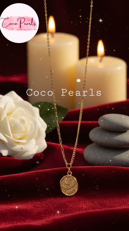 Coco Pearls Stainless Steel Anti Tarnish Gold rose charm necklace with a pendant with roe engraved displayed on a red surface with candles and a white rose