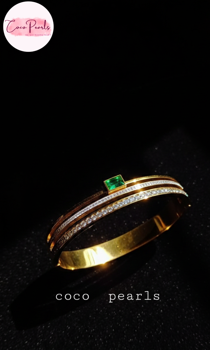 coco pearls stainless steel anti tarnish gold royal emerald diamond handcuff bangle bracelet with rhinestones and emerald in center displayed in dark background