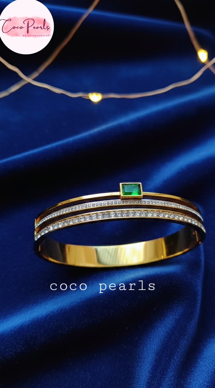 coco pearls stainless steel anti tarnish gold royal emerald diamond handcuff bangle bracelet with rhinestones and emerald in center displayed on a blue background