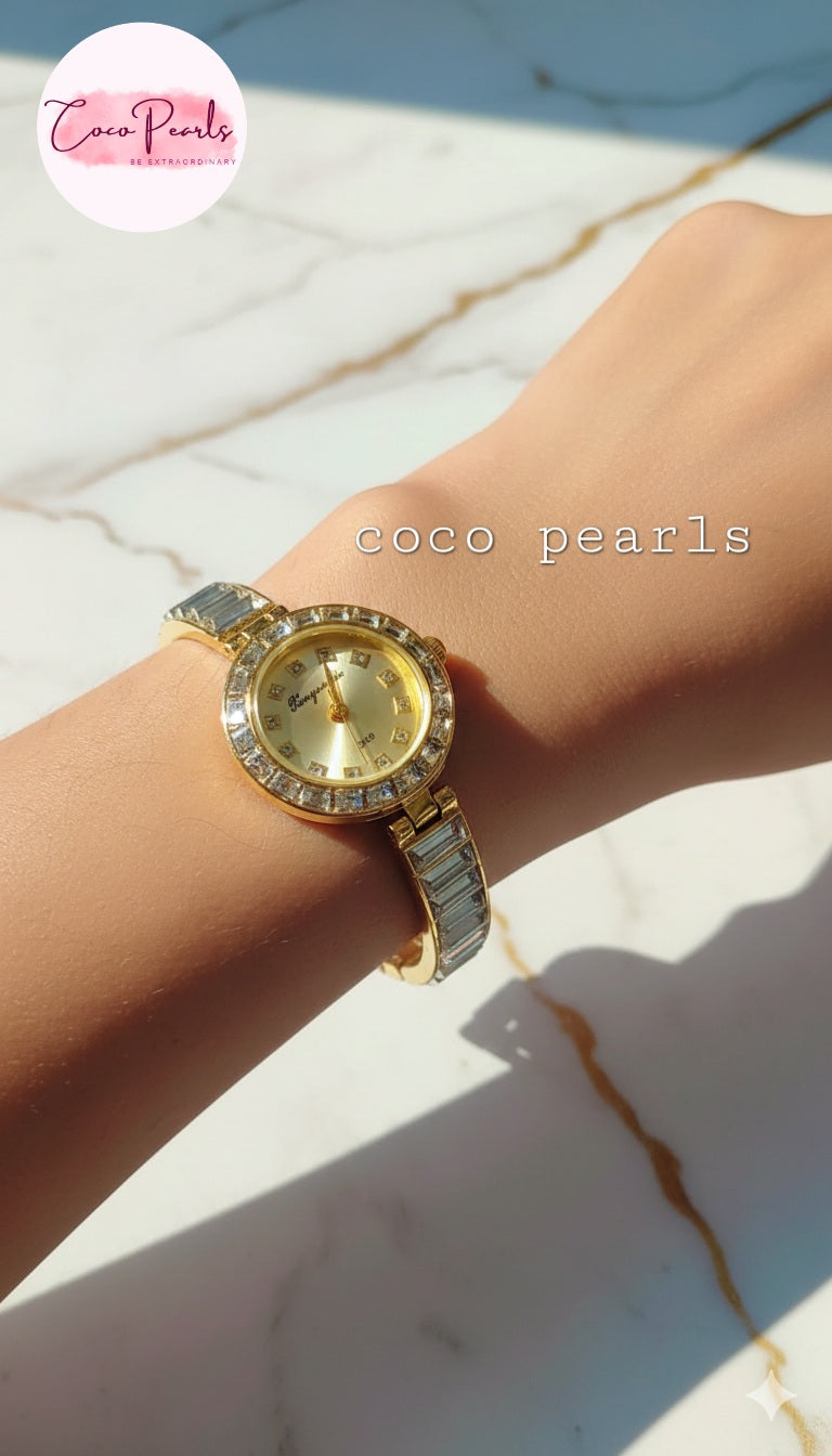 coco pearls Gold watch with rhinestone accents on a wrist against a marble background.