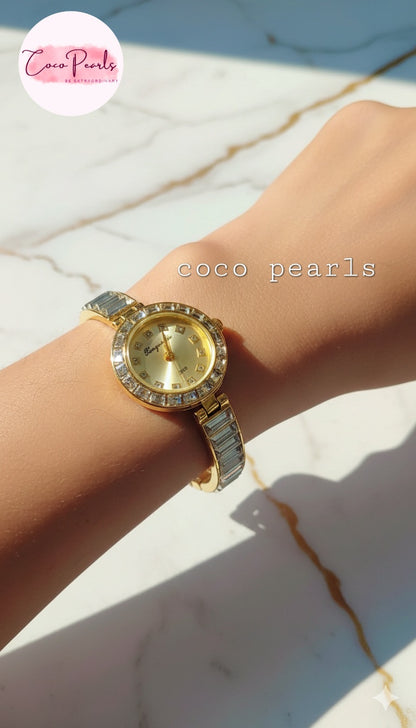coco pearls Gold watch with rhinestone accents on a wrist against a marble background.