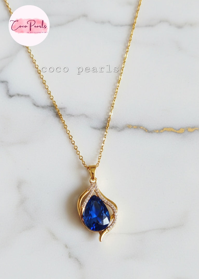coco pearls stainless steel anti tarnish Gold sapphire tear drop necklace with a sapphire blue teardrop pendant on a marble background