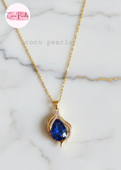 coco pearls stainless steel anti tarnish Gold sapphire tear drop necklace with a sapphire blue teardrop pendant on a marble background