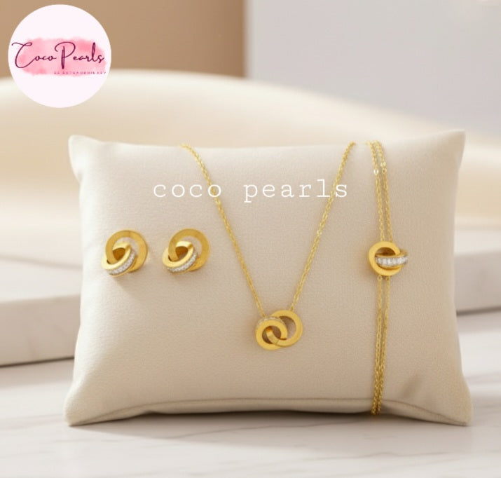 Coco Pearls Stainless Steel Anti tarnish Gold sparkle loop jewelry set with diamond studded necklace, earrings, and bracelet on a white pillow 
