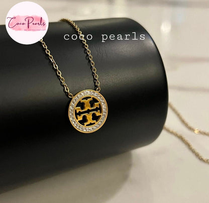Coco Pearls Stainless Steel Anti tarnish Gold sparkly vibe necklace with a circular pendant with diamonds around on a black cylindrical stand