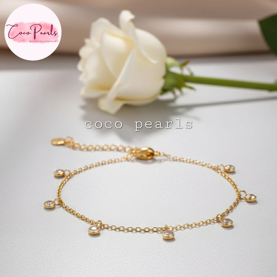 Coco Pearls Stainless steel anti tarnish Gold bracelet with diamonds hanging charms displayed on a light surface with a white rose in the background