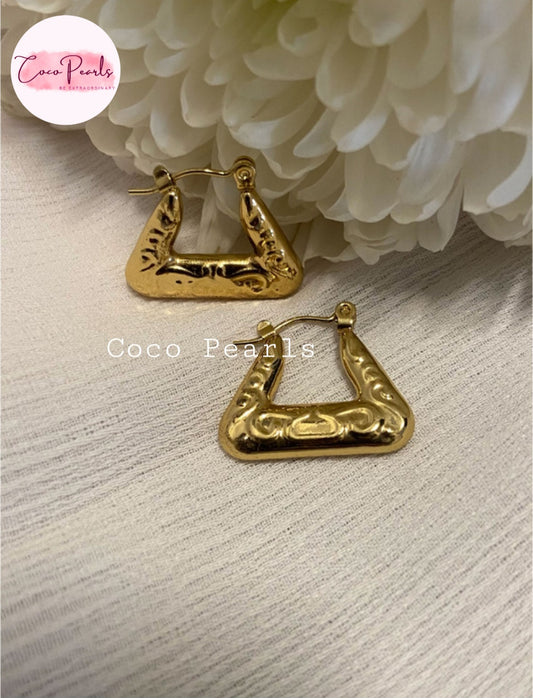 Coco Pearls Stainless Steel Anti Tarnish Gold triangle hoop earrings on a textured surface with white flowers in the background